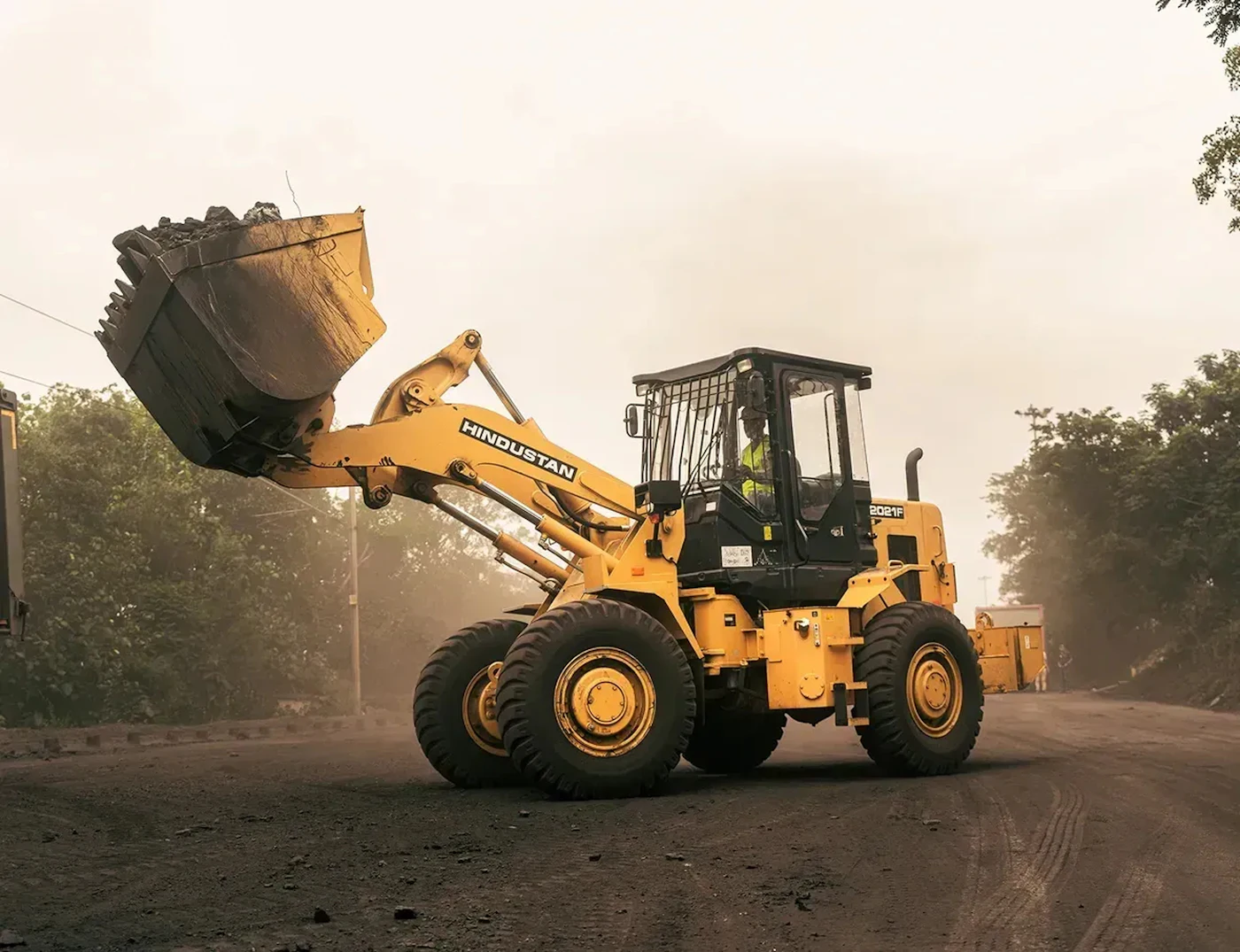 Front-end loader with its bucket raised on a dusty site road